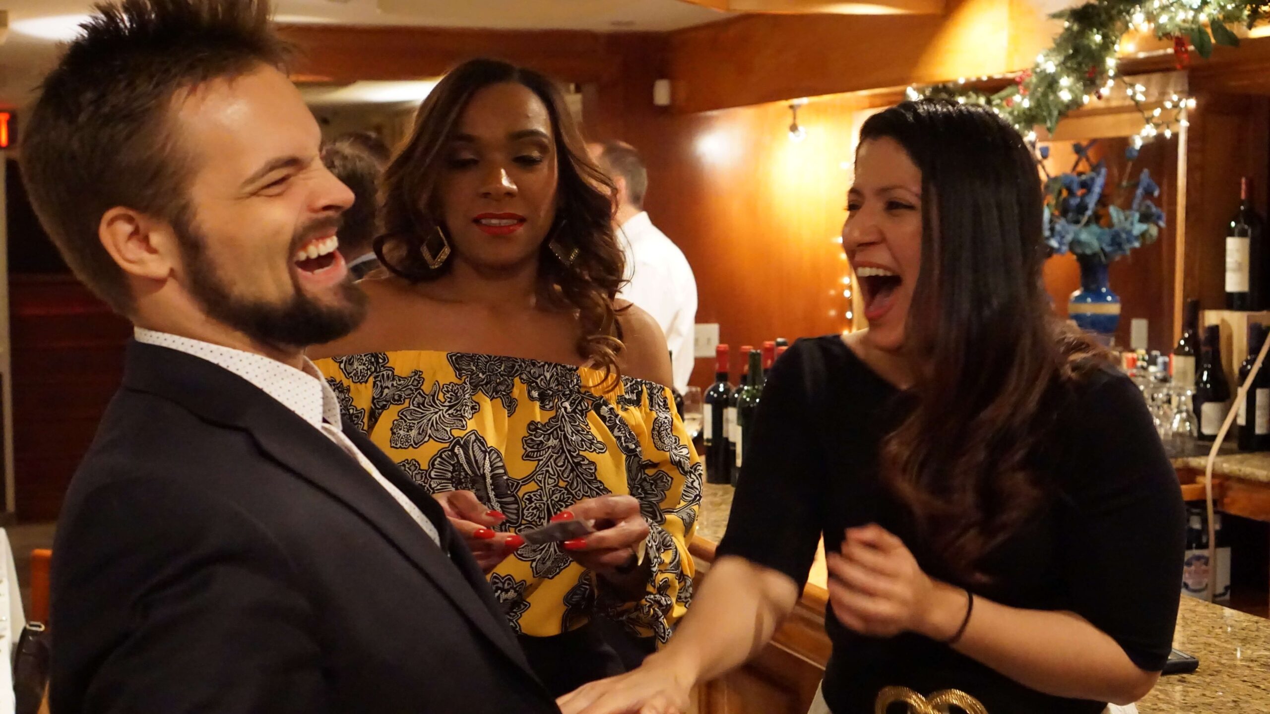 Kent Axell performing close-up magic for two laughing guests at a bar