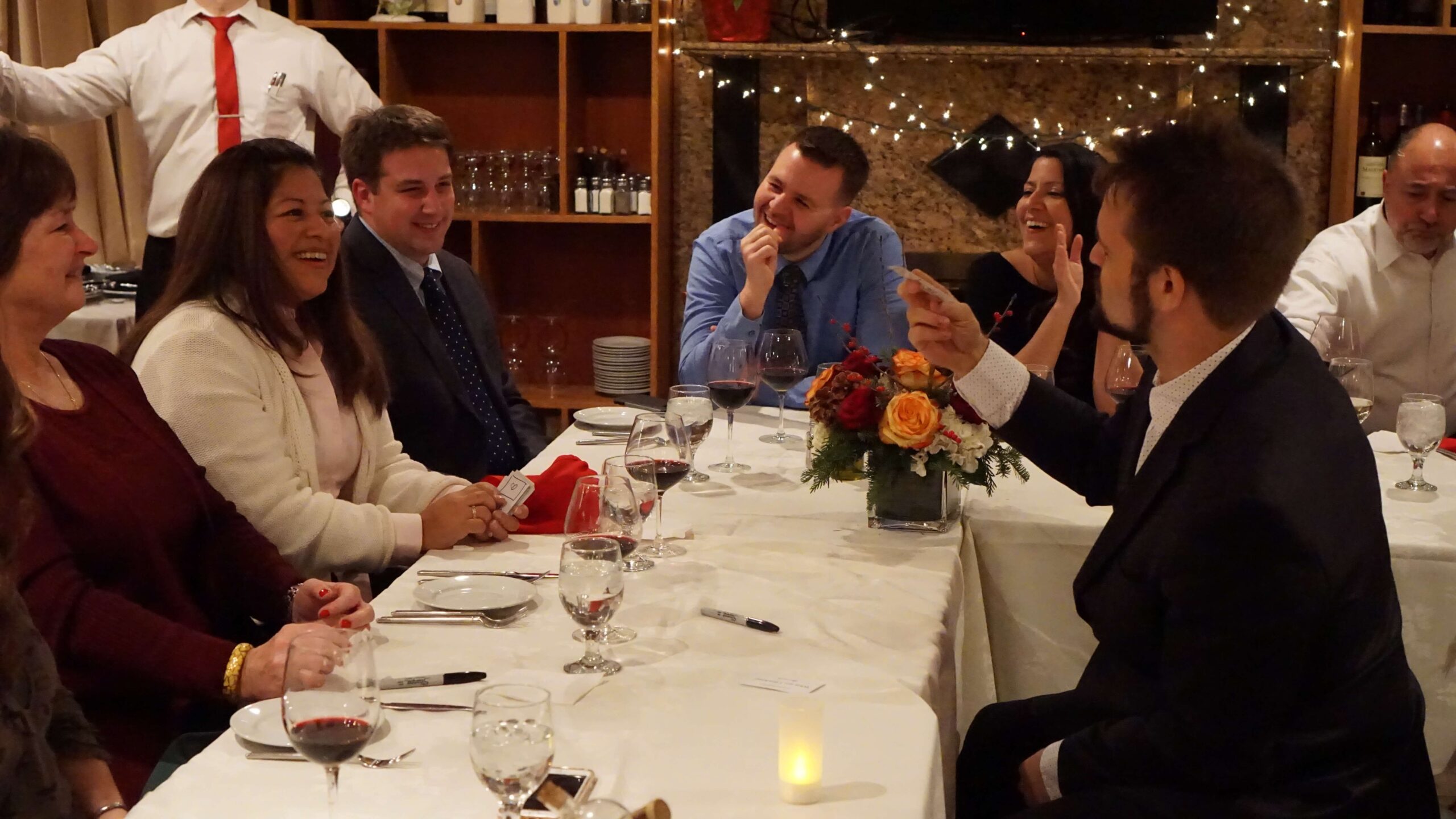 A dinner table of guests reacting to a card revelation