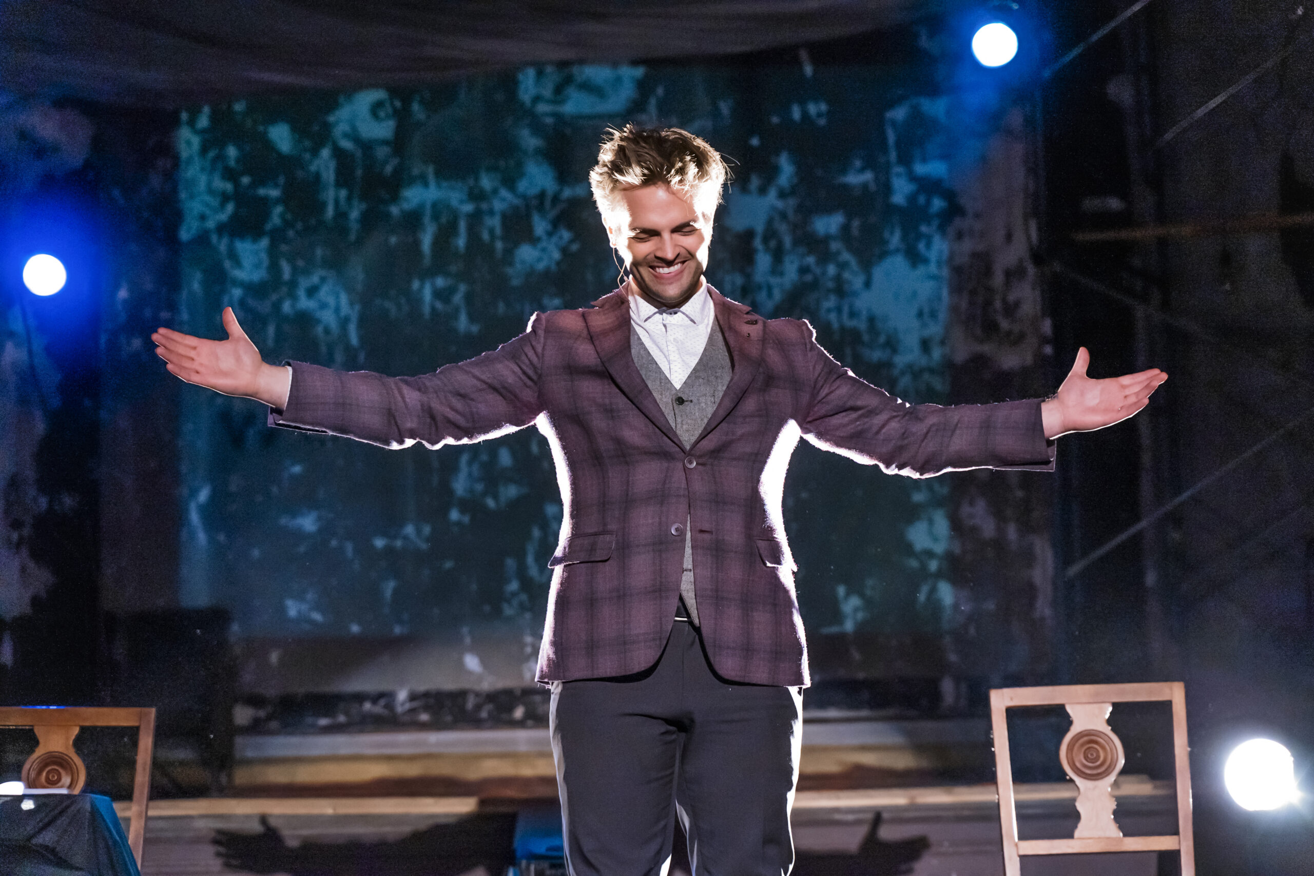 Kent Axell on stage with arms outstretched under blue theatrical light