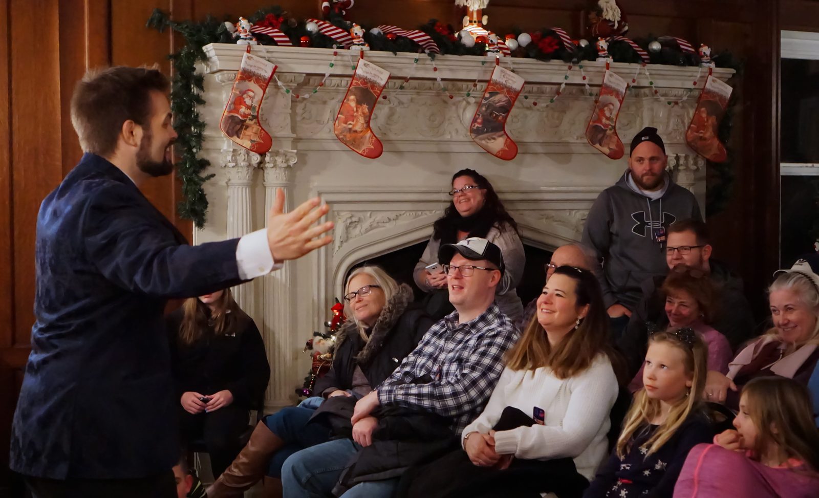 Kent Axell performing for a seated audience beside a decorated fireplace